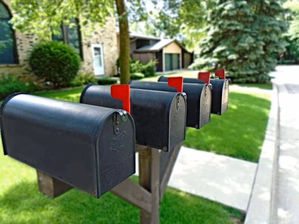A row of black curbside mailboxes with red flags raised on a suburban street