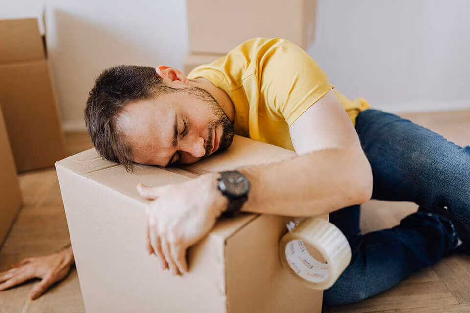 A man slumped asleep over a cardboard box on the floor