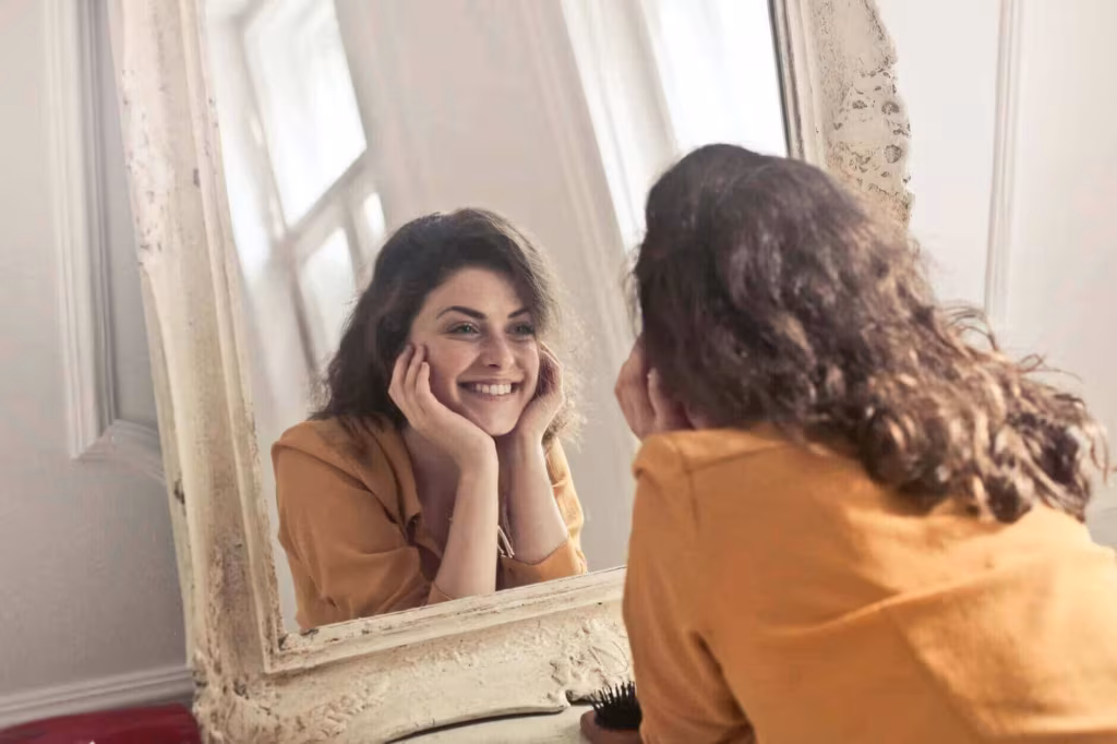 A woman resting her chin on her hand and looking at her reflection in an ornate mirror