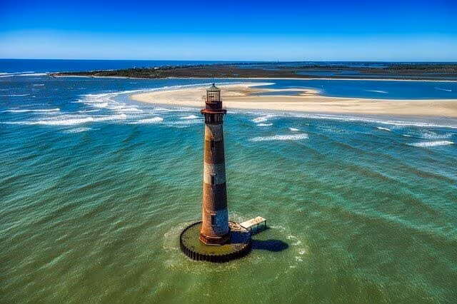A lighthouse standing in shallow turquoise water off a sandbar