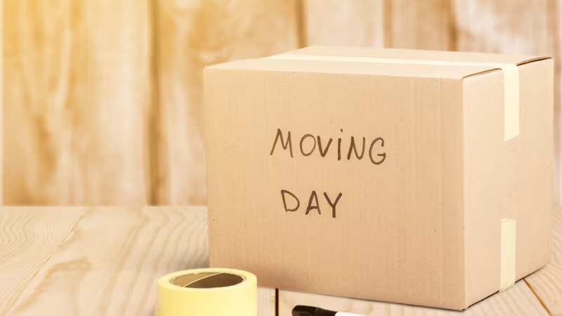 A cardboard box labeled Moving Day beside a roll of tape and a marker pen
