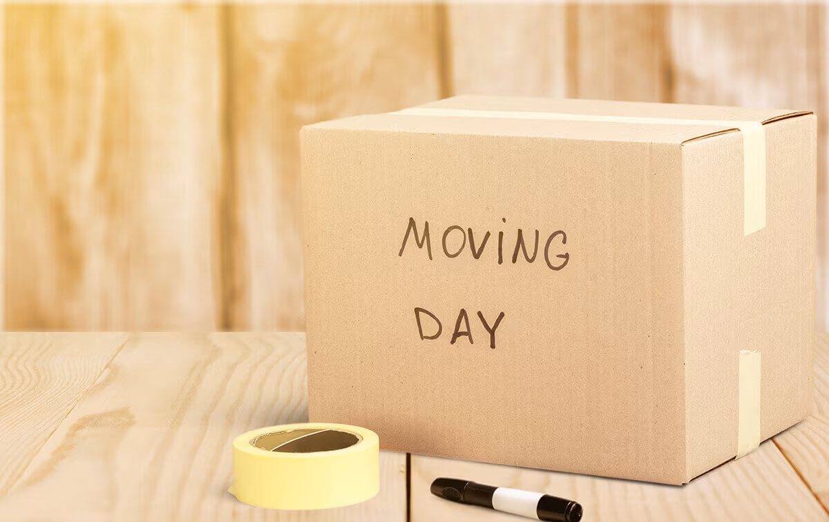 A cardboard box labeled Moving Day beside a roll of tape and a marker pen