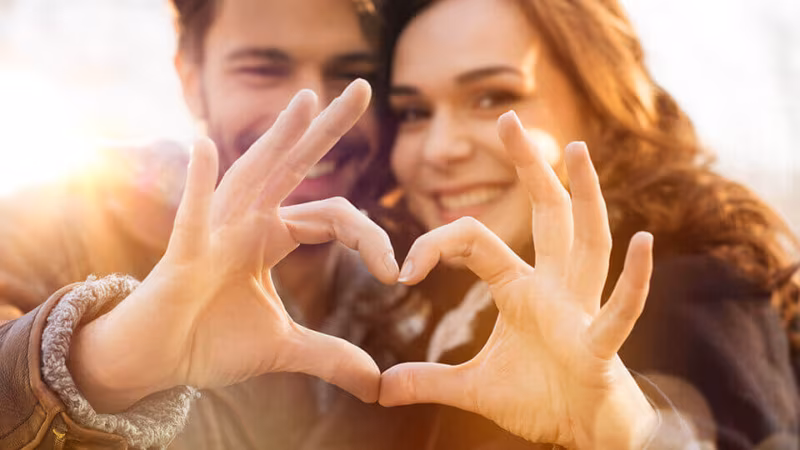 A couple making a heart shape with their hands in front of their faces