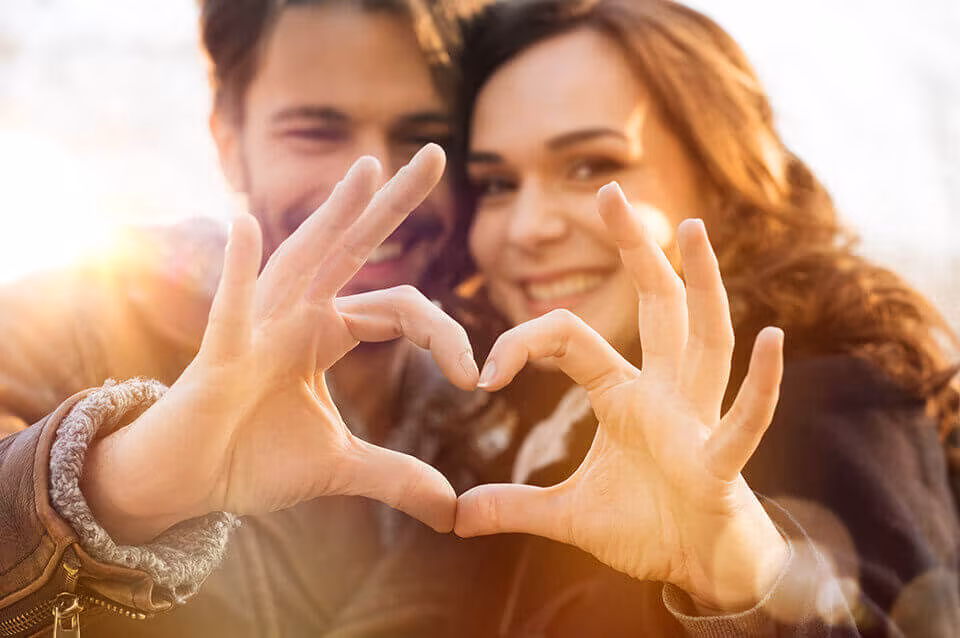 A couple making a heart shape with their hands in front of their faces