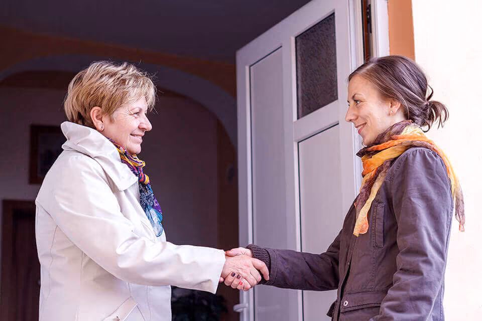 Two women shaking hands at a front door