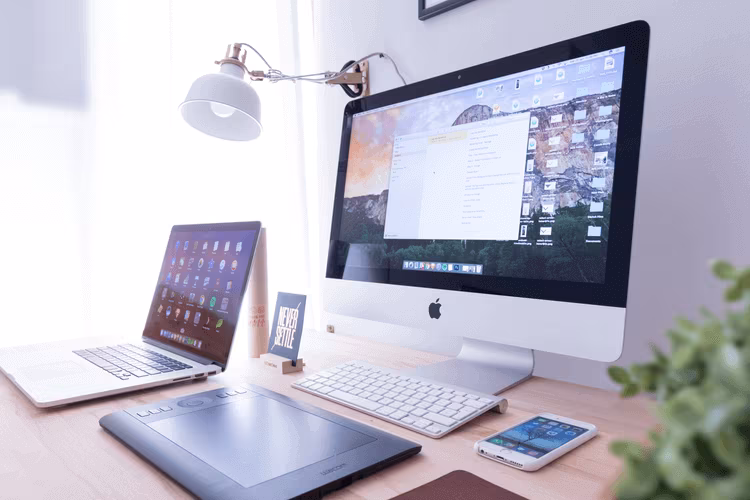 A desk with a desktop computer, a laptop, a keyboard and a phone