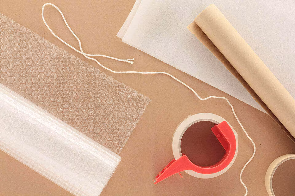 Bubble wrap, kraft paper, twine and a red tape dispenser laid out on a brown surface