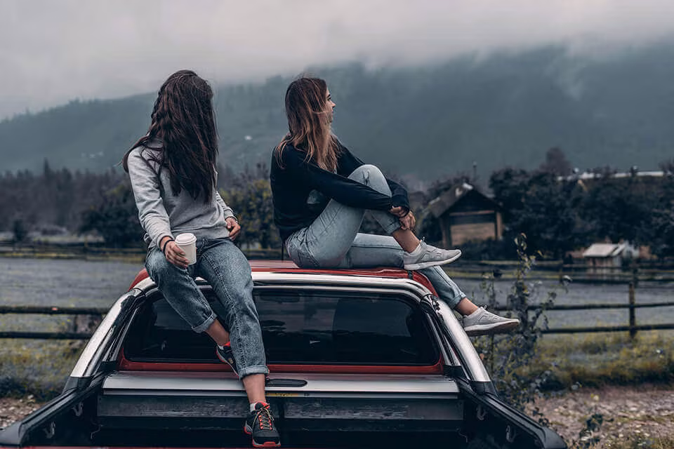 Two people sitting on the open tailgate of a pickup truck with mountains behind them