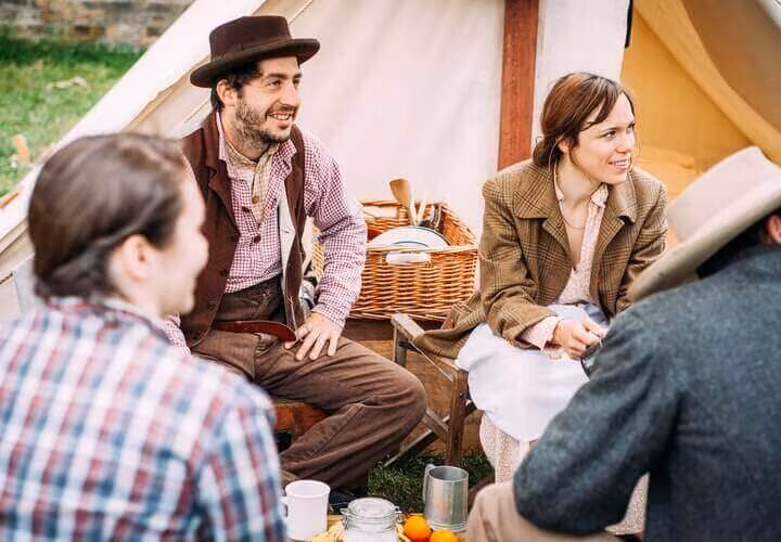 People sitting and talking outside a canvas tent with a picnic basket