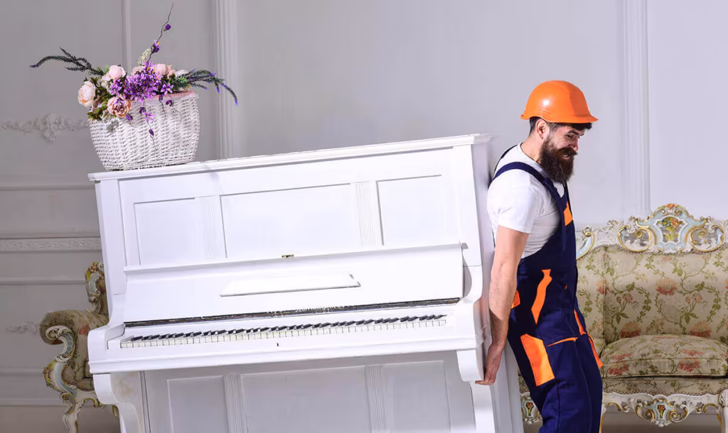 A mover in overalls and a hard hat moving a white upright piano