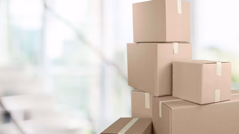 A stack of taped cardboard boxes beside a window