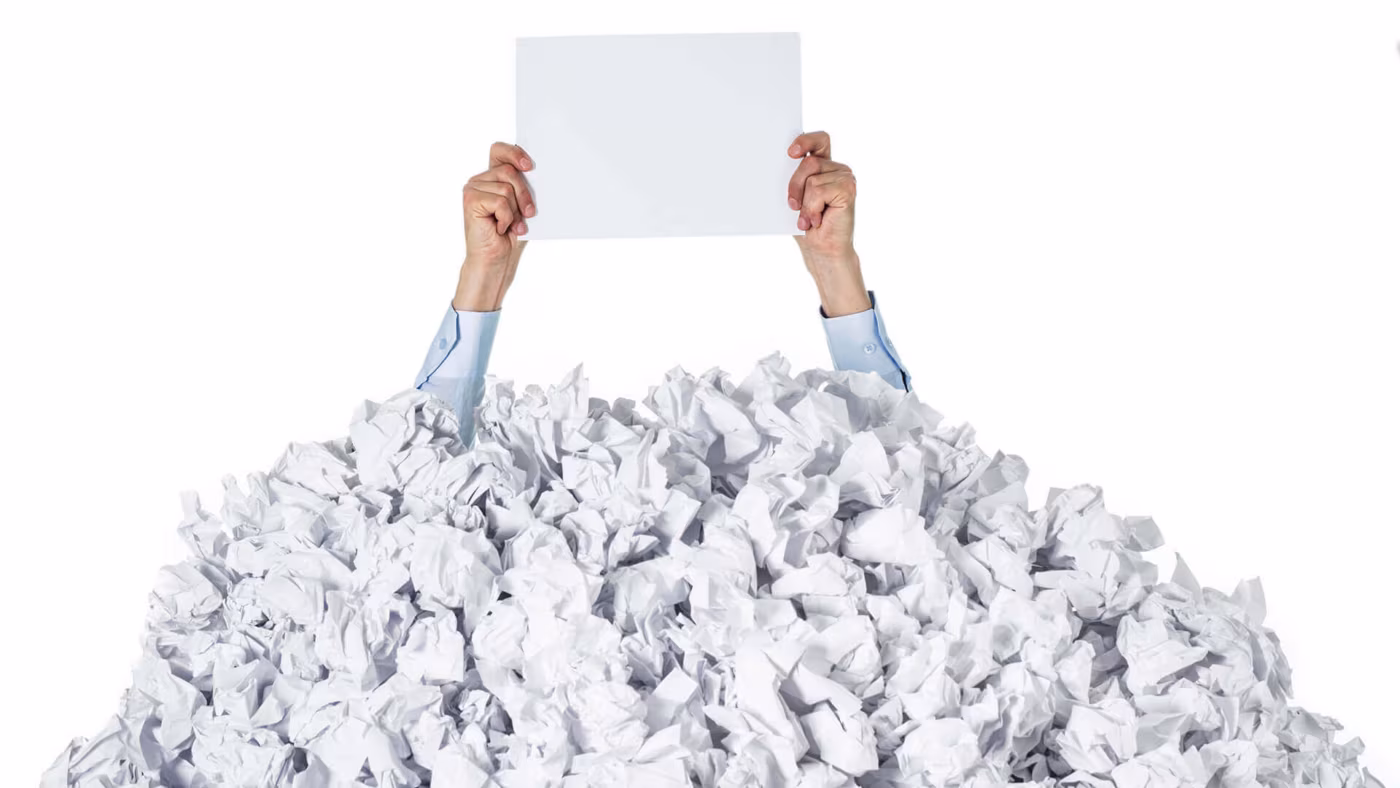 Hands holding a blank sheet of paper above a huge pile of crumpled paper