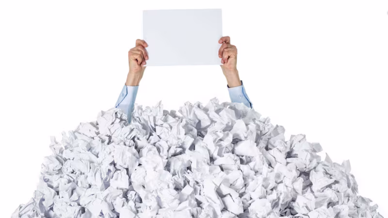 Hands holding a blank sheet of paper above a huge pile of crumpled paper
