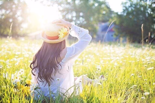 A woman in a sun hat standing in a meadow of tall grass and wildflowers