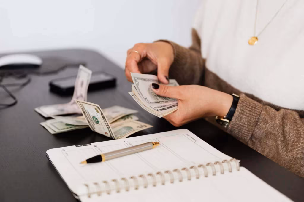 Hands counting banknotes over an open notebook and a pen