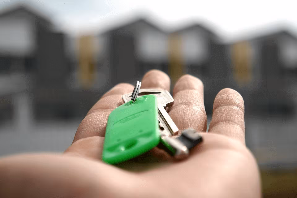 An open palm holding a key with a green fob in front of apartment buildings