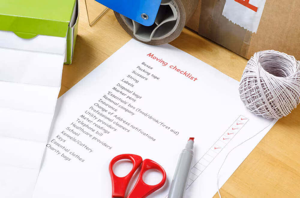 A printed moving checklist beside scissors, twine, a marker and a roll of tape