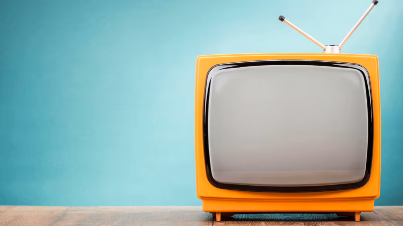 An orange retro television against a turquoise wall