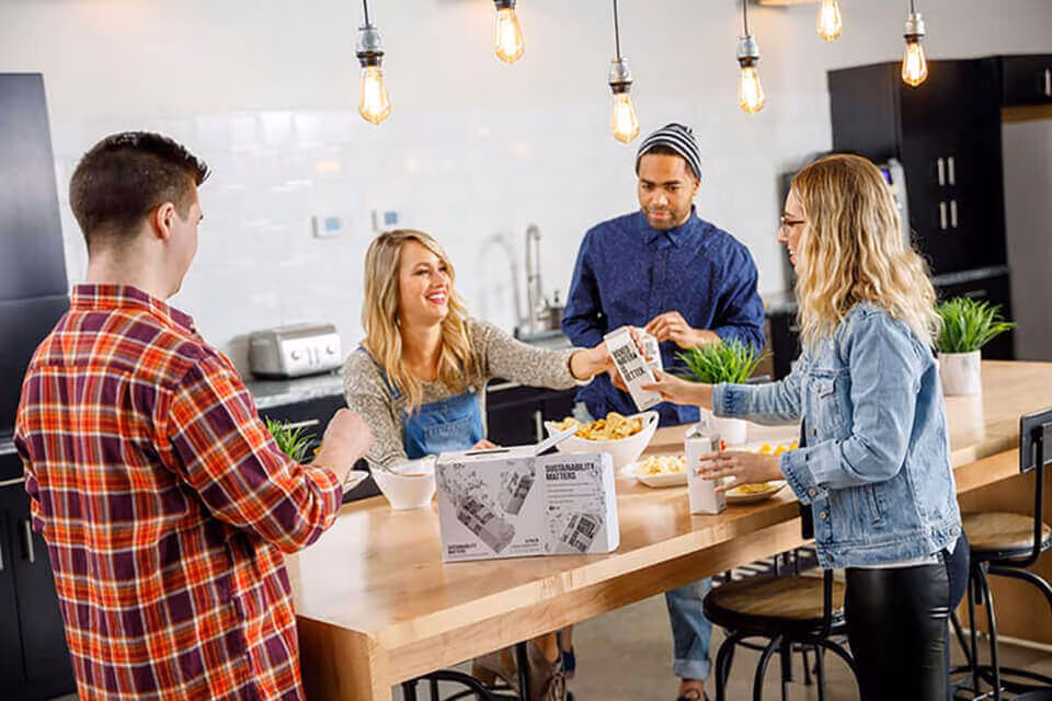 Four people standing around a kitchen island with food and drinks, talking