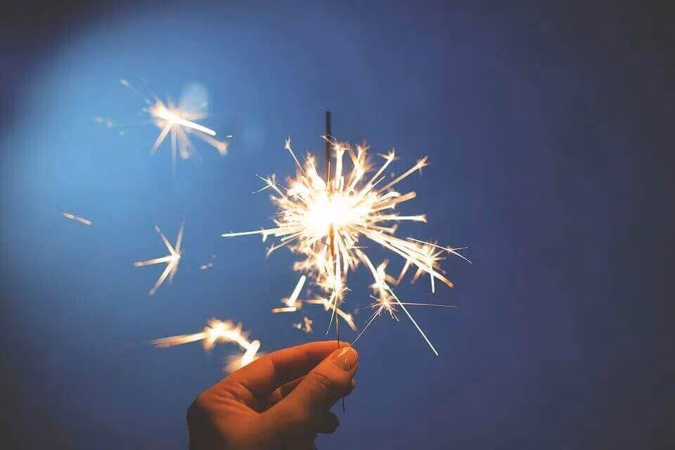 A hand holding a lit sparkler against a dark blue background