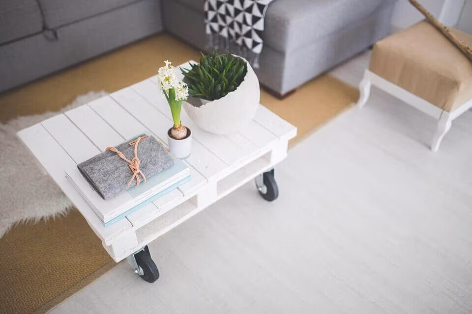 A white pallet coffee table on castors holding a plant and books, beside a grey sofa