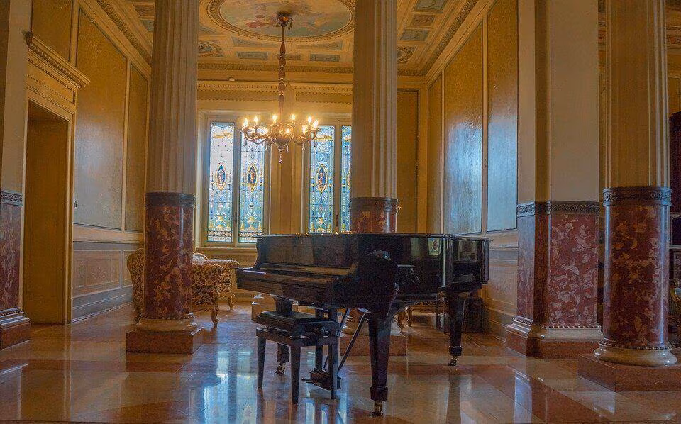 A grand piano in an ornate hall with marble columns, a chandelier and a polished floor