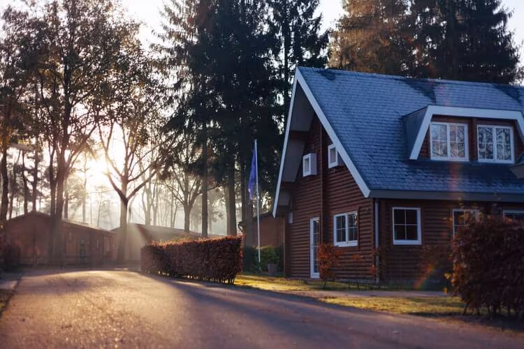 A dark timber house set back from a quiet tree-lined road at dusk