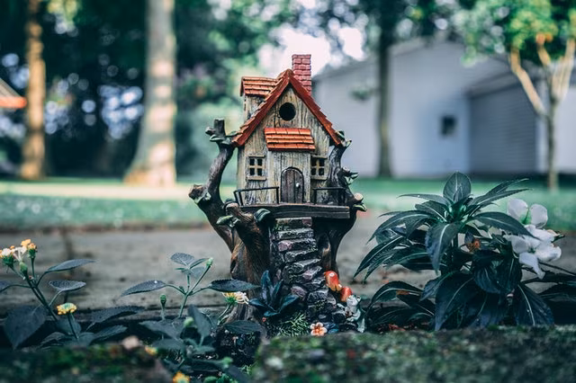 A miniature house model standing in a garden among plants