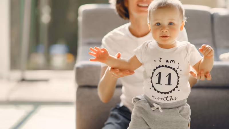 A woman holding a baby's hands as it takes a step in a living room
