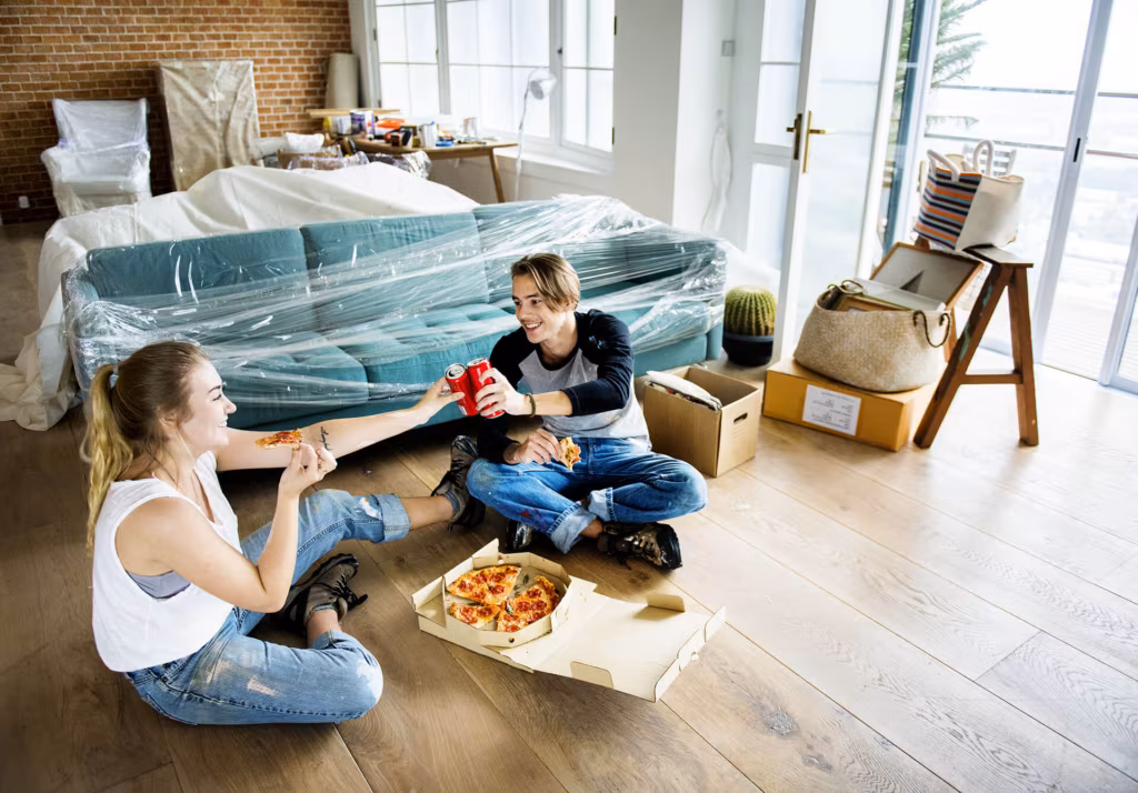 A couple sitting on the floor, eating pizza after cross-country moving