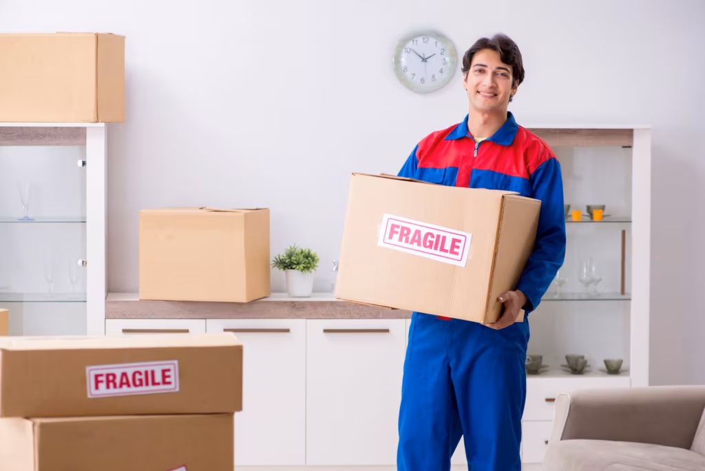 Professional mover carefully carrying a labeled fragile box during a home relocation.