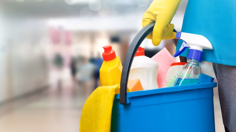 A blue bucket of cleaning bottles held by a gloved hand