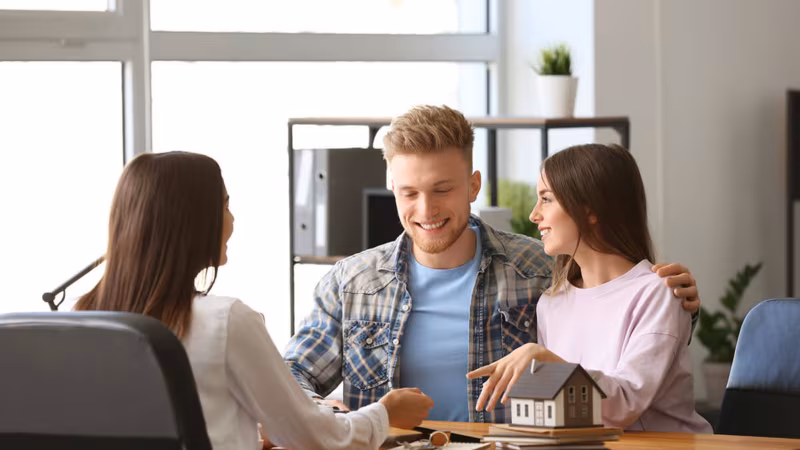 Three people talking across a desk with a model house on it