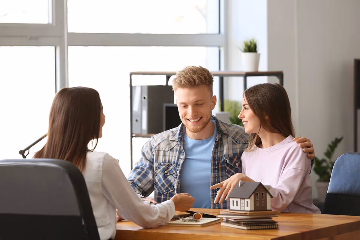 Three people talking across a desk with a model house on it