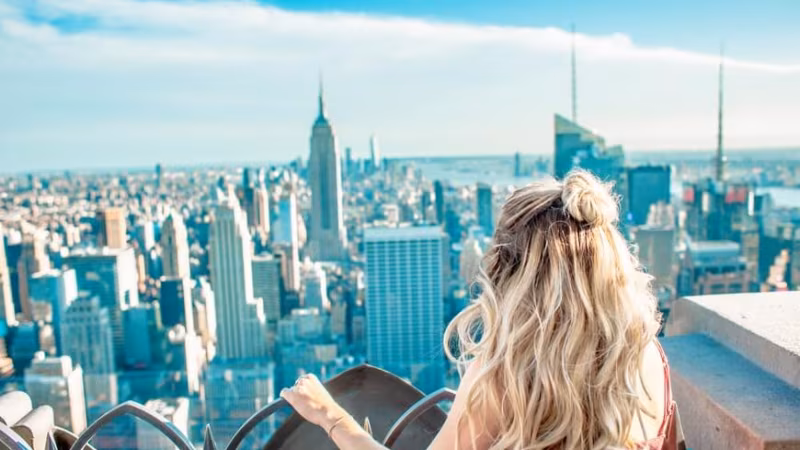 A woman with her arms raised looking out over the Manhattan skyline