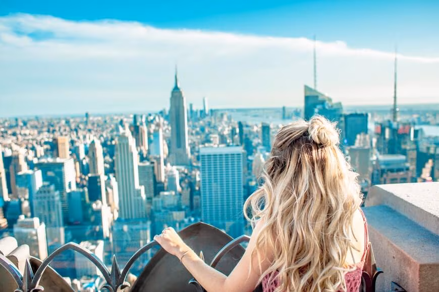 A woman with her arms raised looking out over the Manhattan skyline