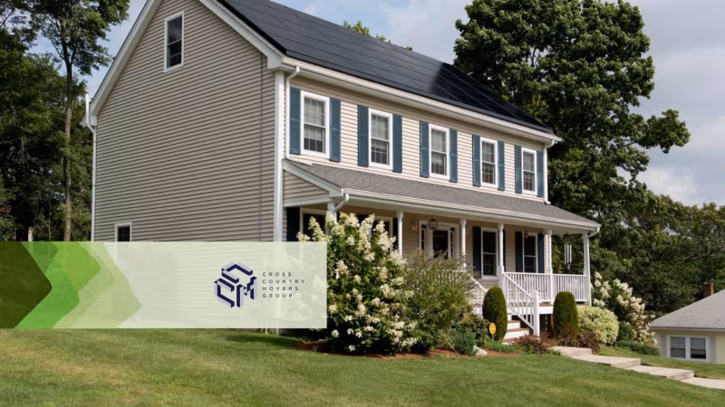 A two-storey grey clapboard house with a mown lawn and flowering shrubs
