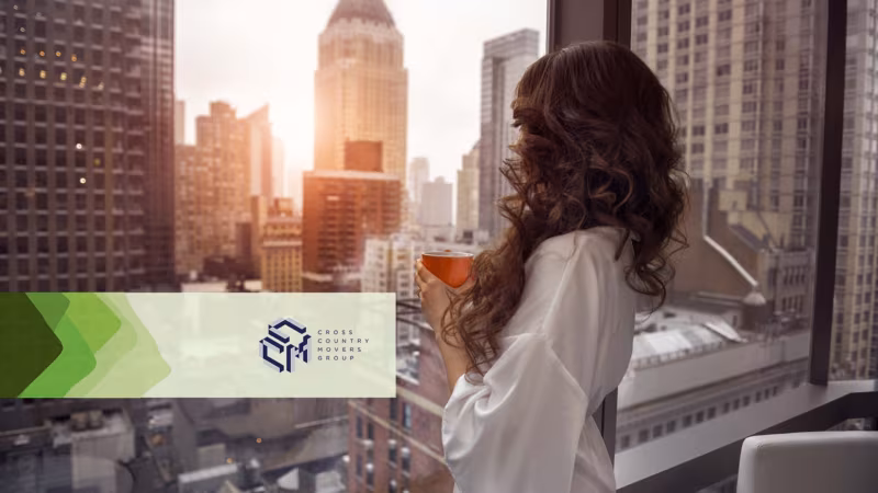 A woman holding a drink at a high window overlooking a city skyline