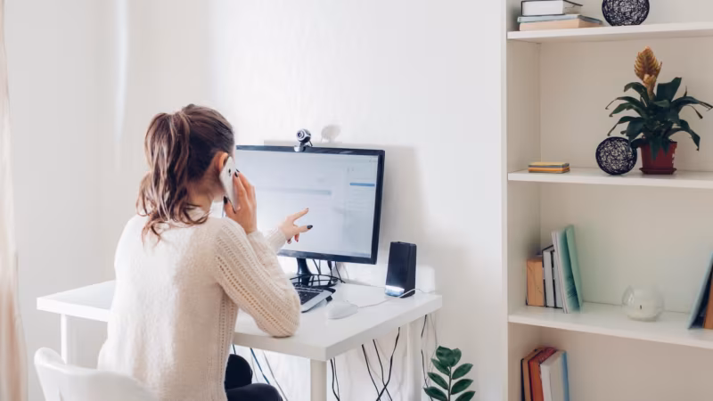 A woman talking on the phone in front of a computer