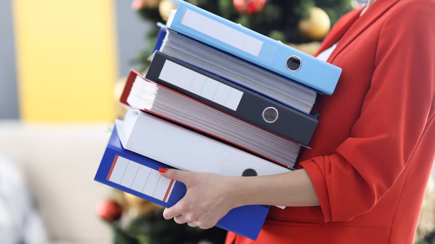 A person carrying a stack of ring binders and folders