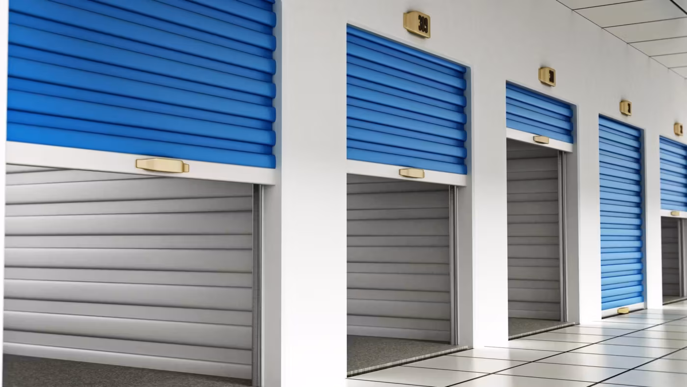 A lit corridor between two runs of blue roller doors inside a building