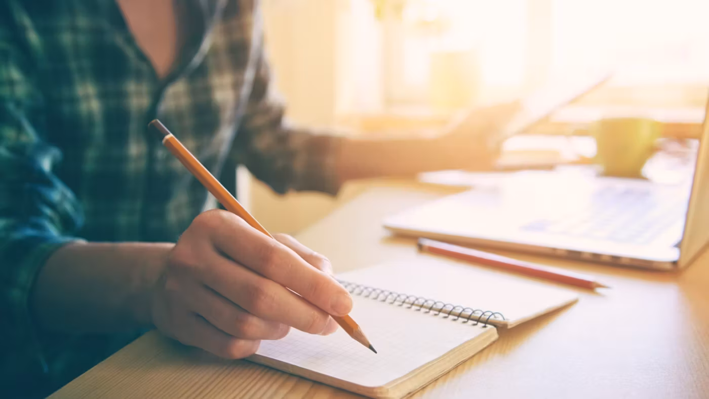 A hand writing on a pad at a sunlit desk