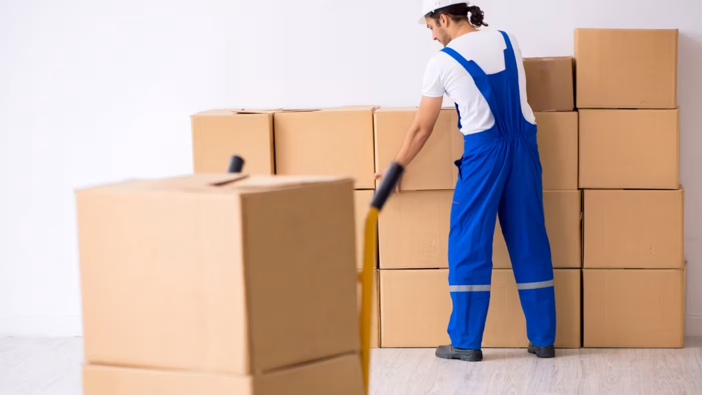 A mover with a hand truck beside a wall of stacked cartons