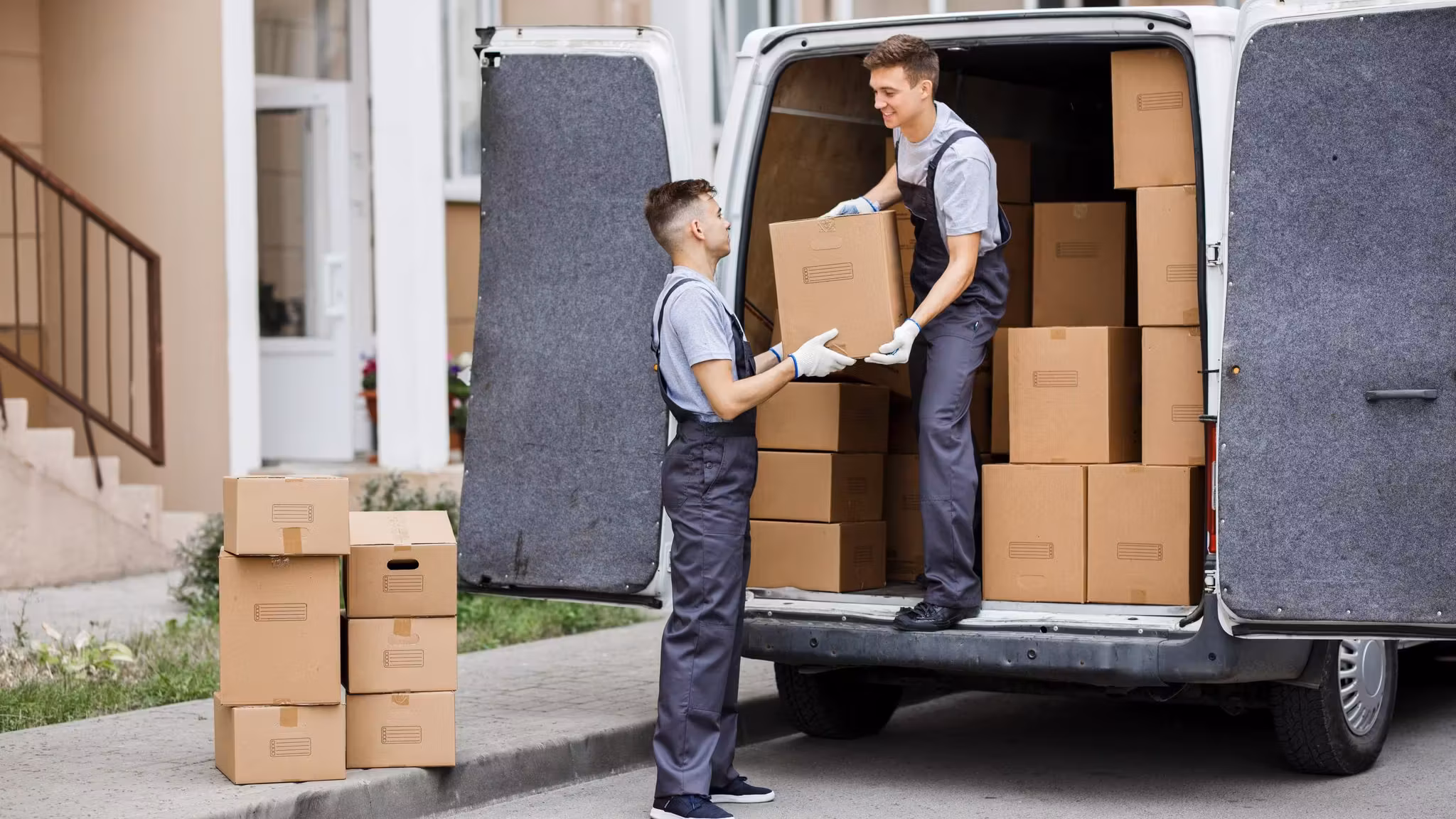 Two movers unloading cartons from a van parked at the curb of a residential street