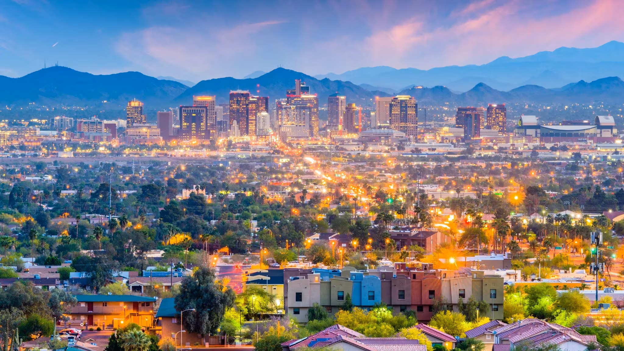 The Phoenix valley at dusk, homes in the foreground and mountains behind the lit city