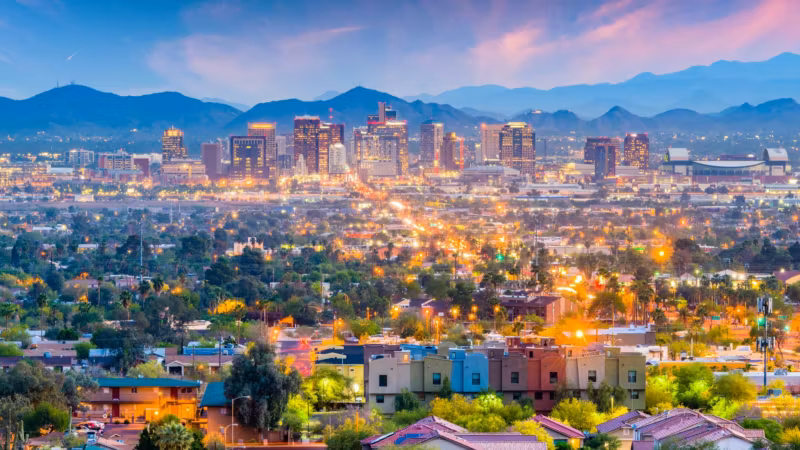 The Phoenix valley at dusk, homes in the foreground and mountains behind the lit city