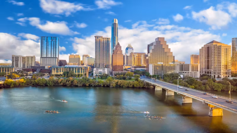 The Austin skyline above Lady Bird Lake, with a road bridge and rowers on the water