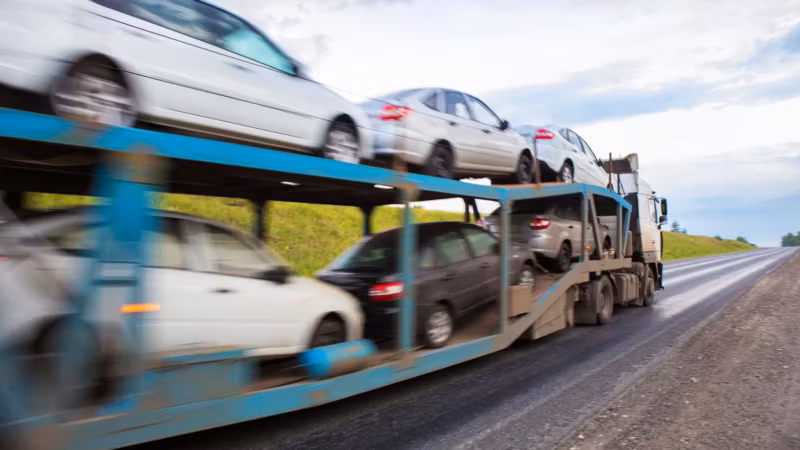 A car carrier in motion on a highway, the vehicles blurred by speed