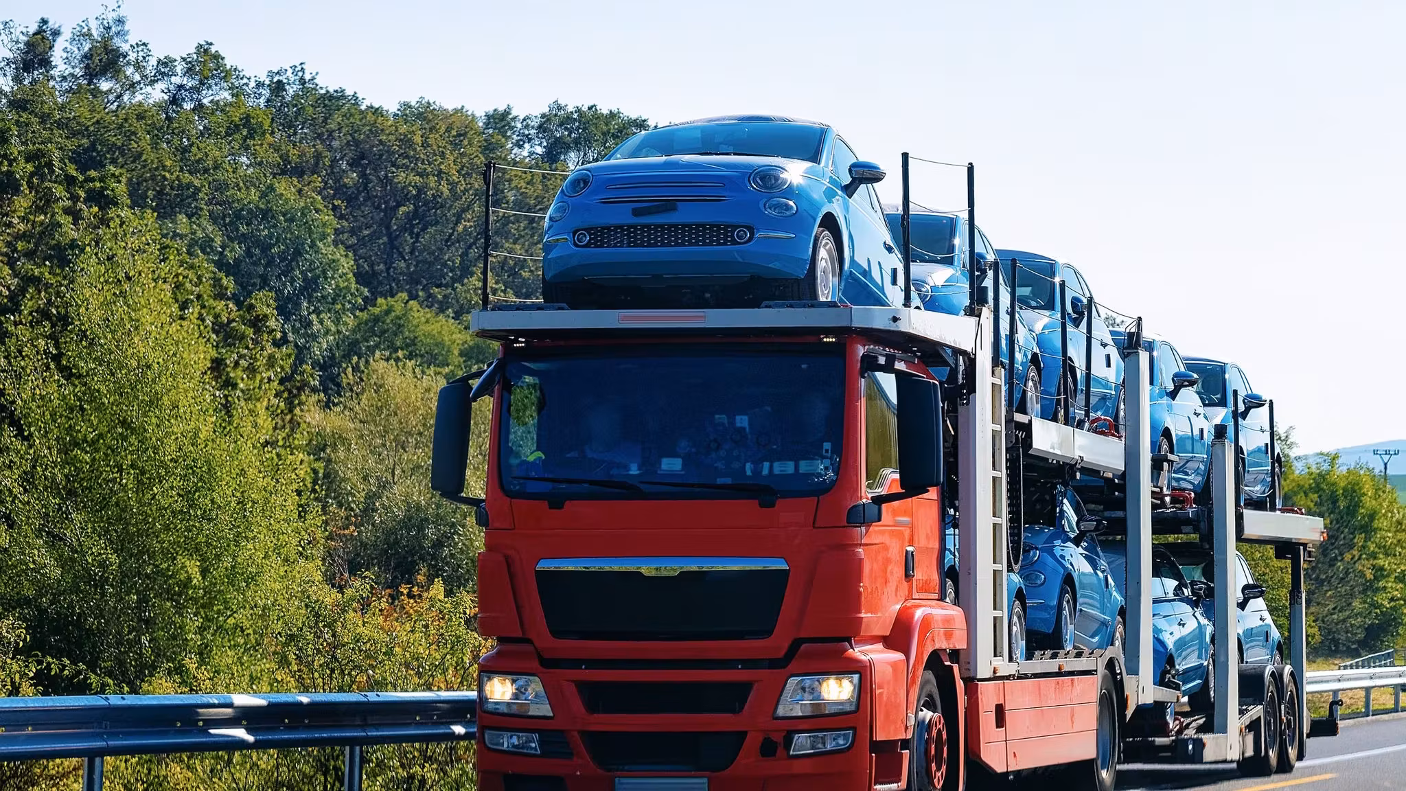 A red tractor unit hauling a loaded car carrier along a highway