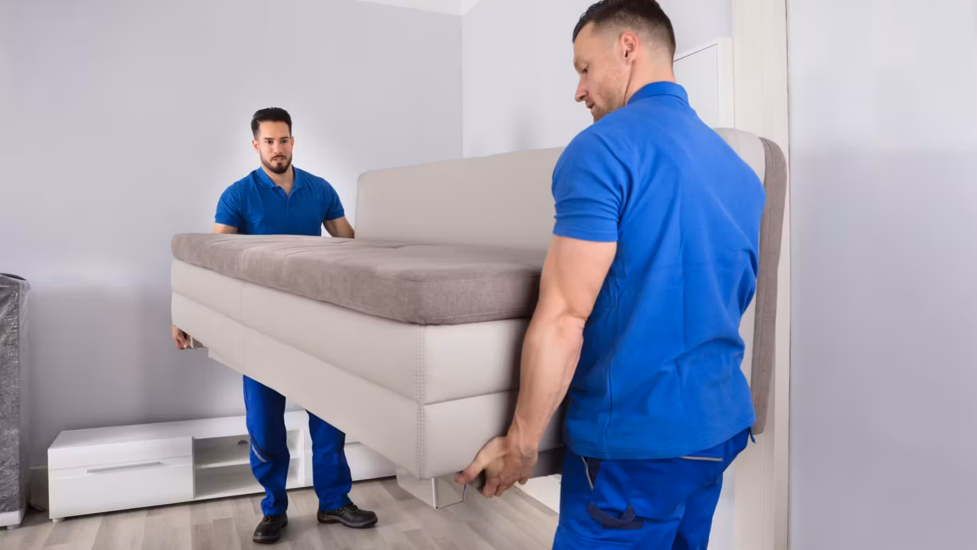 Two movers lifting a sofa between them in a bare room